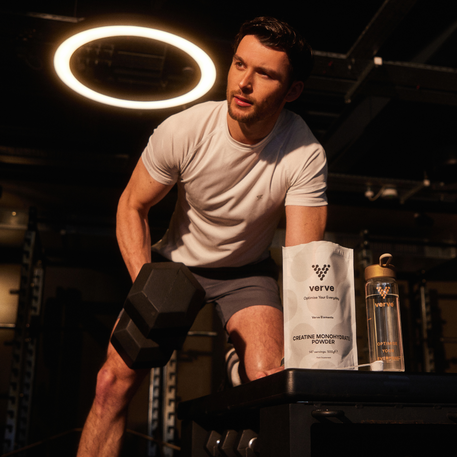 Man lifting a dumbbell in a gym, with Verve Creatine Monohydrate Powder and water bottle on a bench in front of him.
