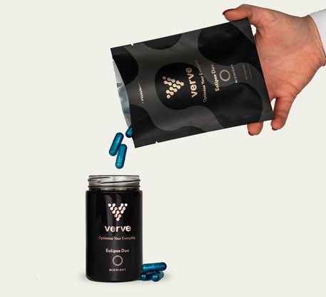 A hand pours blue capsules from a Verve Eclipse Duo Midnight refill pouch into a matching black jar, with some capsules on the surface below.