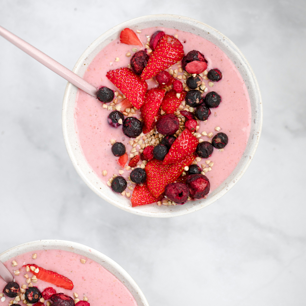 Pink yoghurt bowl topped with strawberries, blueberries and seeds