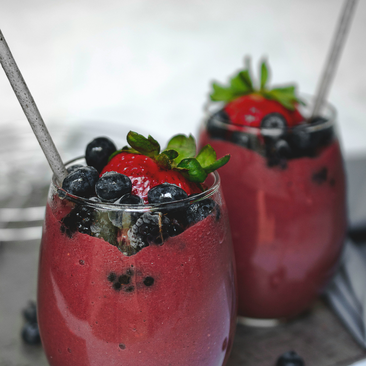 Two glasses of berry smoothie topped with blueberries and strawberries