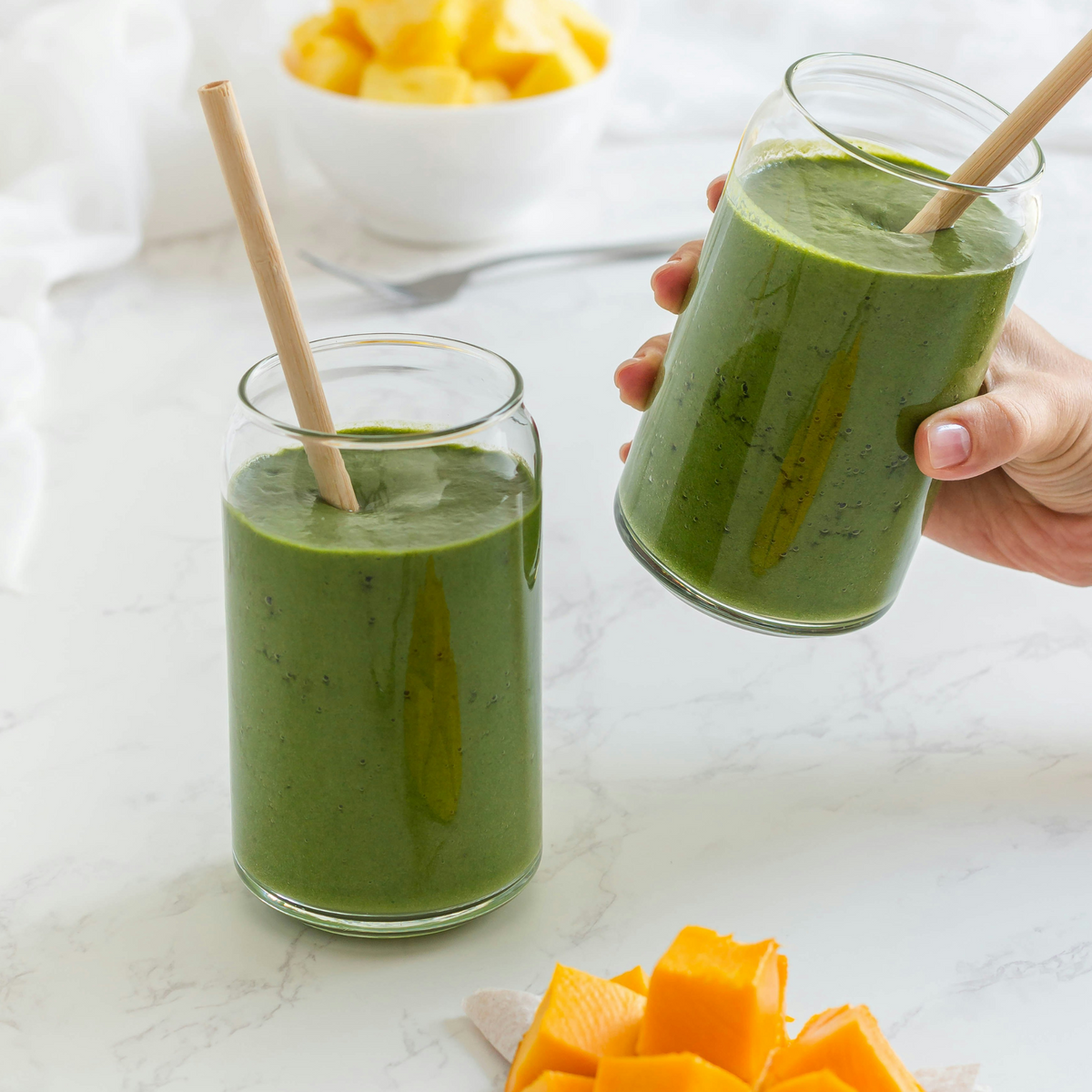 Two glasses of green mango smoothie with paper straws and mango chunks