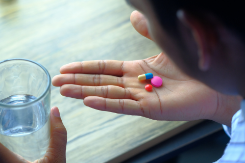 A hand holding capsules next to a glass of water