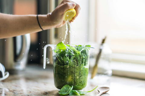 Lemon being squeezed into a jug of blended green leaves on a kitchen counter
