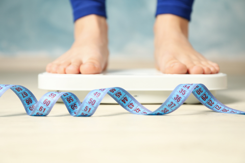 Bare feet on bathroom scales next to a tape measure