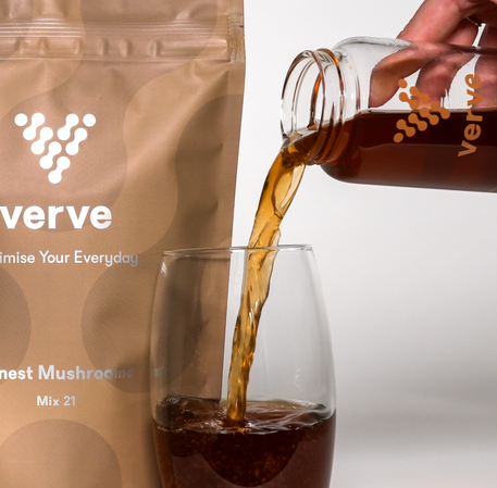 A hand pours a dark liquid from a Verve-branded bottle into a glass, next to a Verve Honest Mushrooms Mix 21 pouch.