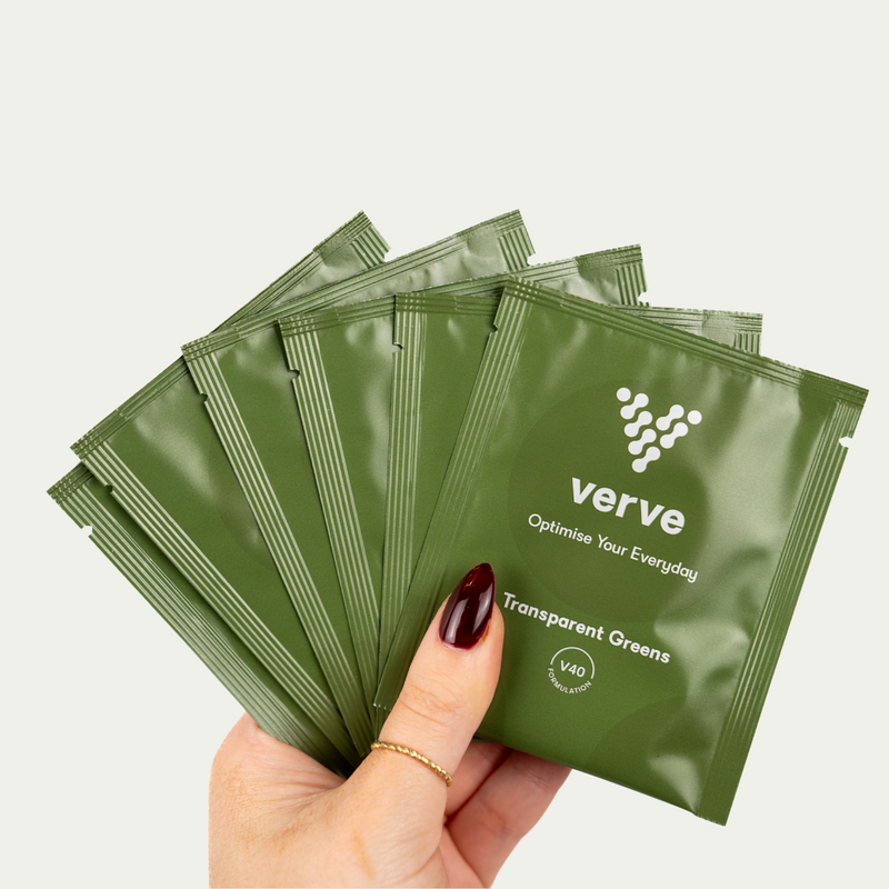 A hand holding six green sachets labelled "verve Transparent Greens – Optimise Your Everyday" against a plain background.