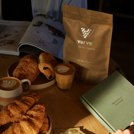Verve Honest Mushrooms pouch placed on a breakfast table alongside croissants, lattes, and a book titled "Mindful Living," evoking a calm and nourishing morning ritual.