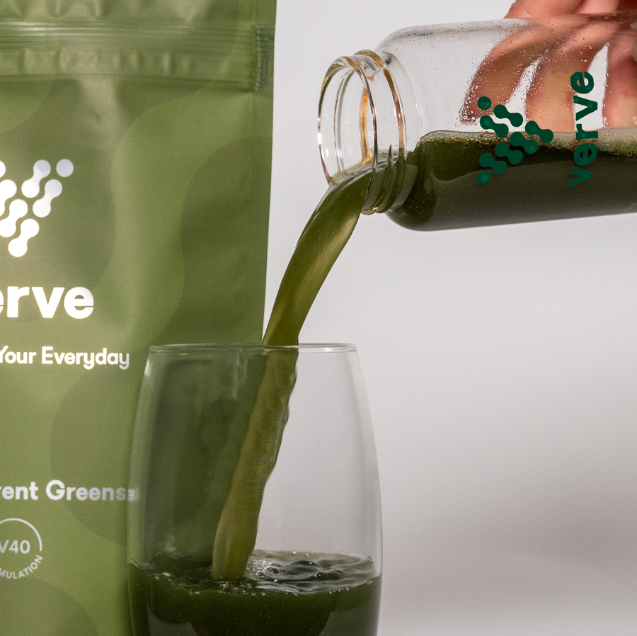 A hand pours a green liquid from a Verve-branded bottle into a glass, beside a Verve Transparent Greens powder pouch.